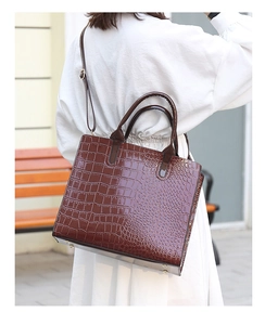 Detail of dark brown crocodile pattern handbag with sturdy handles and adjustable strap