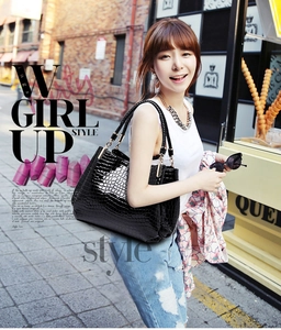 Close-up of black crocodile embossed handbag with gold hardware on a street model