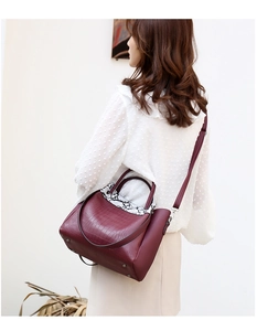 Detail of burgundy crocodile-embossed tote bag with snake print trim and adjustable strap