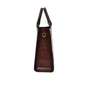 Side view of dark brown crocodile embossed patent leather handbag with metal hardware