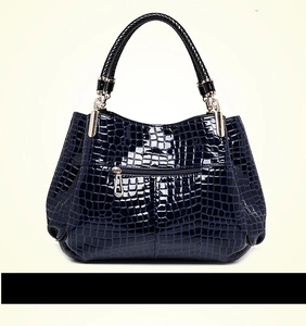 Detail of dark blue crocodile embossed handbag with glossy finish and silver metal buckle