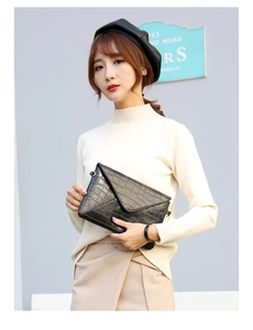 Detail of black crocodile embossed envelope clutch bag held by model in white sweater
