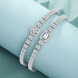 Detail of silver tennis bracelets with round and emerald cut center stones on blue stand