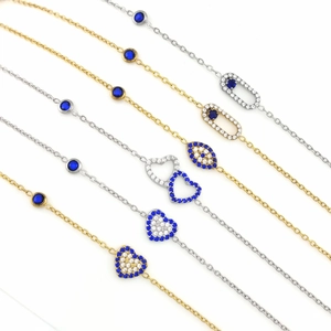 Detalle de pulseras delicadas con corazones de circón y dijes de ojo azul en tono dorado