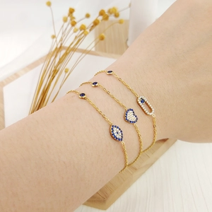 Detalle de tres pulseras bañadas en oro con colgantes de corazón y ojo turco de circonita