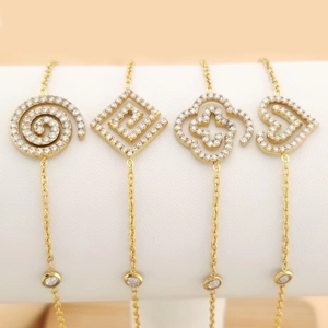 Close-up of four gold bracelets with zircon heart and clover charms on a white stand