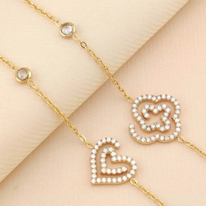 Macro detail of gold stainless steel heart and flower bracelet with pavé-set crystals