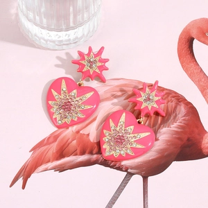 Détail des boucles d'oreilles cœur en émail rose avec cristaux et motifs étoilés