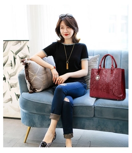 Deep red snakeskin embossed luxury handbag displayed on a blue velvet sofa