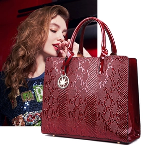 Detail of burgundy snakeskin embossed patent leather tote bag with gold charm