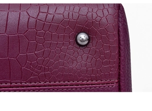 Macro detail of wine red crocodile embossed leather with silver metal studs and stitching
