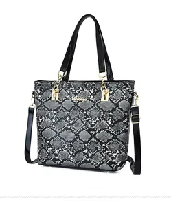 Detail of snake skin print tote bag with black patent leather handles and gold metal accents