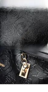 Detail of black pebbled leather handbag with camellia embossing and gold hardware