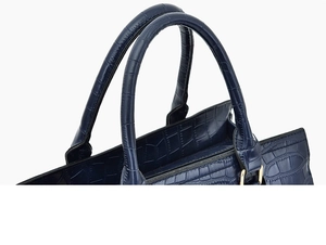 Close-up of crocodile embossed texture on navy blue handbag with gold metal hardware