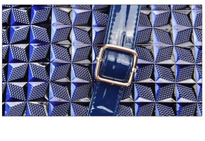 Close-up of geometric embossed patent leather and golden buckle on women's handbag