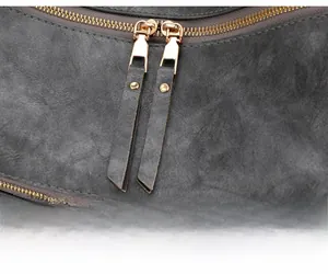 Dettaglio della doppia cerniera dorata con tiranti in pelle su borsa grigio scuro morbida