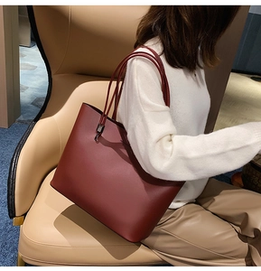 Detailed view of a burgundy leather tote bag held by a model in casual chic attire