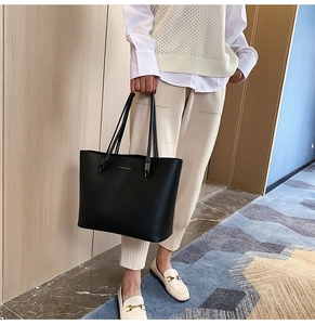 Detail of a large black leather tote bag with Forever Young text on casual model