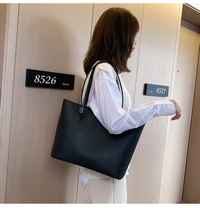 Minimalist black leather tote bag with long handles styled in a modern hallway setting