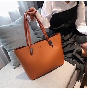 Close-up of brown leather tote bag with Forever Young gold text on a grey sofa