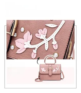 Detail of floral embroidery and pearl accents on a light pink faux leather handbag
