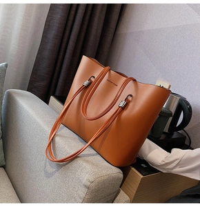 Close-up of brown leather tote bag with Forever Young text on a grey sofa