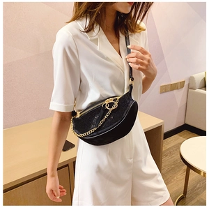 Detail of a crescent rhinestone crossbody bag with gold chain worn on a white blazer