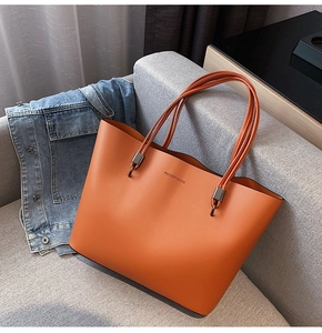 Detail of tan leather tote bag with Forever Young embossing on a soft grey sofa
