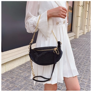 Detail of a black crescent rhinestone chest bag with gold chain on a white dress