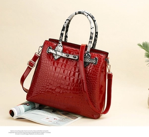 Detail of red croc-embossed handbag featuring snakeskin pattern handles and gold hardware