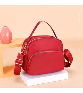 Detail view of red waterproof nylon crossbody bag with gold zippers and multiple layers