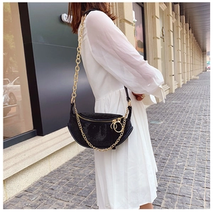Detail of a black rhinestone crescent bag with gold chain strap on a white dress