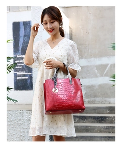 Detail of red crocodile pattern handbag with golden H charm and snake print handle