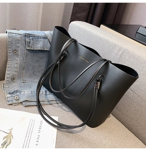 Detail of black leather tote bag with gold Forever Young lettering on a grey sofa