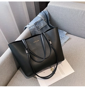 Classic black tote bag in pebbled leather with gold lettering displayed on a sofa