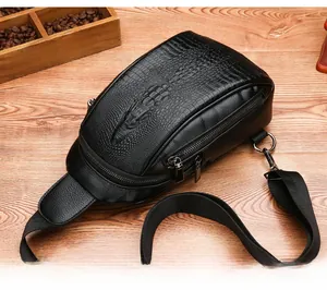 Close-up of black crocodile embossed men's chest bag with metal zipper on wooden table