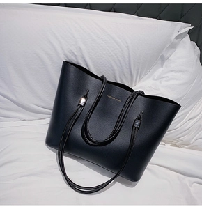 Detail of black leather tote bag with Forever Young gold logo on a white pillow background