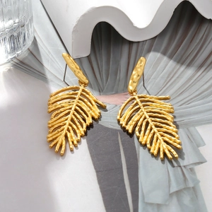 Close-up of golden textured leaf drop earrings on a modern minimalist magazine background