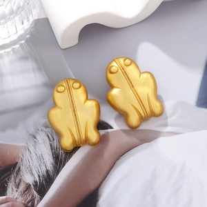 Retro frog stud earrings with matte gold finish on fashion magazine background
