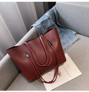 Detail of burgundy leather tote bag with Forever Young embossing on a soft grey sofa