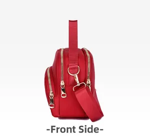 Side view of red nylon crossbody bag showing three layered gold-tone metal zippers