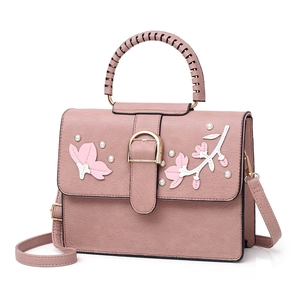 Pink faux leather handbag with 3D floral embroidery and pearl accents on white background