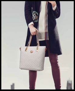 Close-up of white tote bag with arrow pattern print and circular metallic logo detail