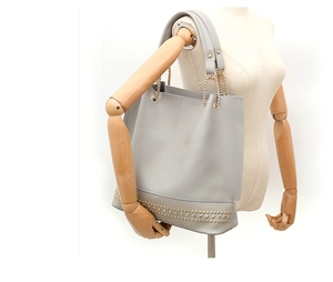 Detail der grauen Shopper-Tasche mit Goldnieten und Kettenhenkel am Holzmodell