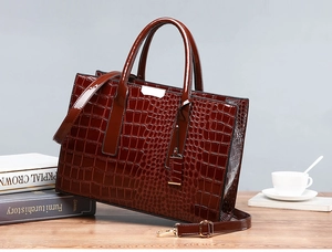 Detail einer burgunderroten Handtasche mit Krokodilprägung, Doppelgriffen und Metallbeschlag