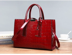 Detailansicht weinroter Shopper mit Krokoprägung und Gold-Hardware auf Holztisch