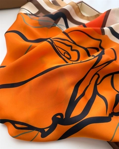 Close-up of luxury silk scarf showing abstract black floral patterns on vibrant orange satin