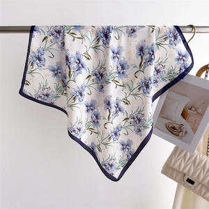 Close-up of floral silk scarf with blue trim hanging on a metal rod with a bag