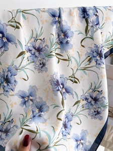 Detailed view of white silk scarf with vibrant blue floral patterns and fine blue edges