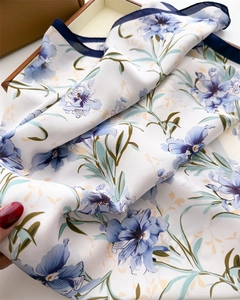 Detailed macro view of vibrant blue floral prints on a white silk scarf with rolled edges